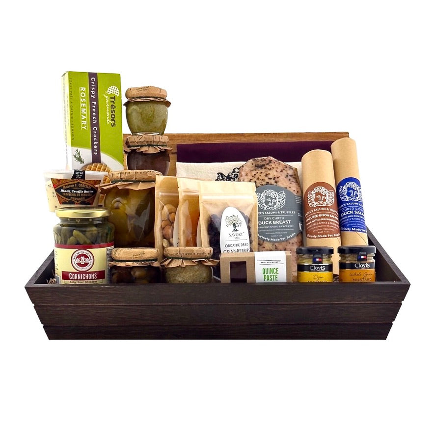 A wooden gift basket box containing various pork-free charcuterie items including duck salami, bison salami, dried apricots, organic dried cranberries, cashews, quince paste, mustards, cornichons, and olives.